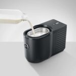 Zwart melkopschuimer met melk die wordt toegevoegd, ideaal voor koffie en cappuccino's, compact en gebruiksvriendelijk keukenapparaat.