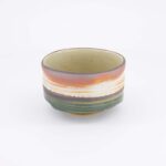 Handgemaakte keramische kom met kleurrijke strepen in aardetinten, perfect voor servies en decoratie.