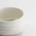 Witte keramische kom met eenvoudige, strakke ontwerp op een witte achtergrond, perfect voor keuken- en serveeraccessoires.