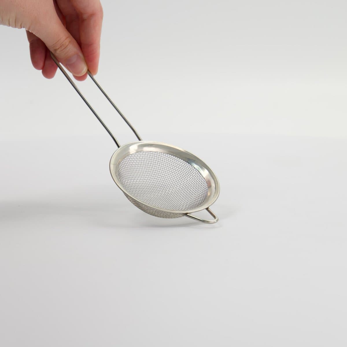 Kleine metalen zeef of sifter voor koken of bakken, handvast gehouden tegen een witte achtergrond.