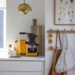 Koffiezetapparaat en accessoires op een witte keukenblad met decoratieve elementen en natuurlijke lichtinval.