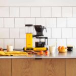 Geel Moccamaster koffiezetapparaat met bijpassende accessoires op een keukenblad.