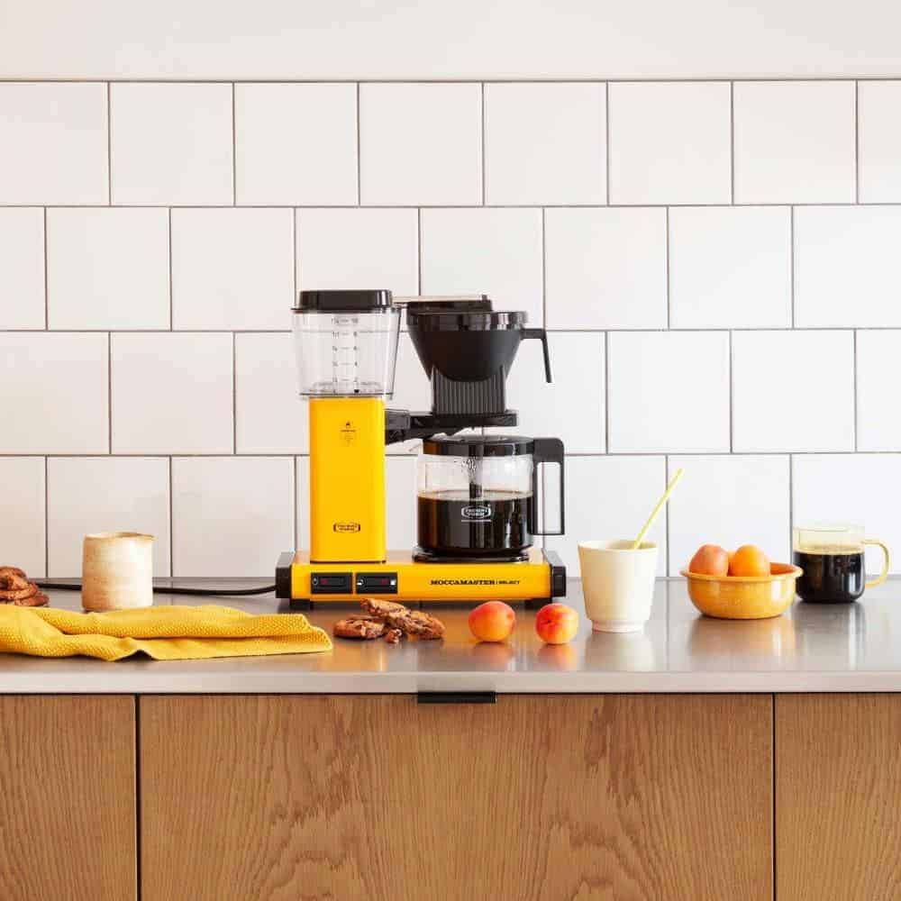 Geel Moccamaster koffiezetapparaat met bijpassende accessoires op een keukenblad.